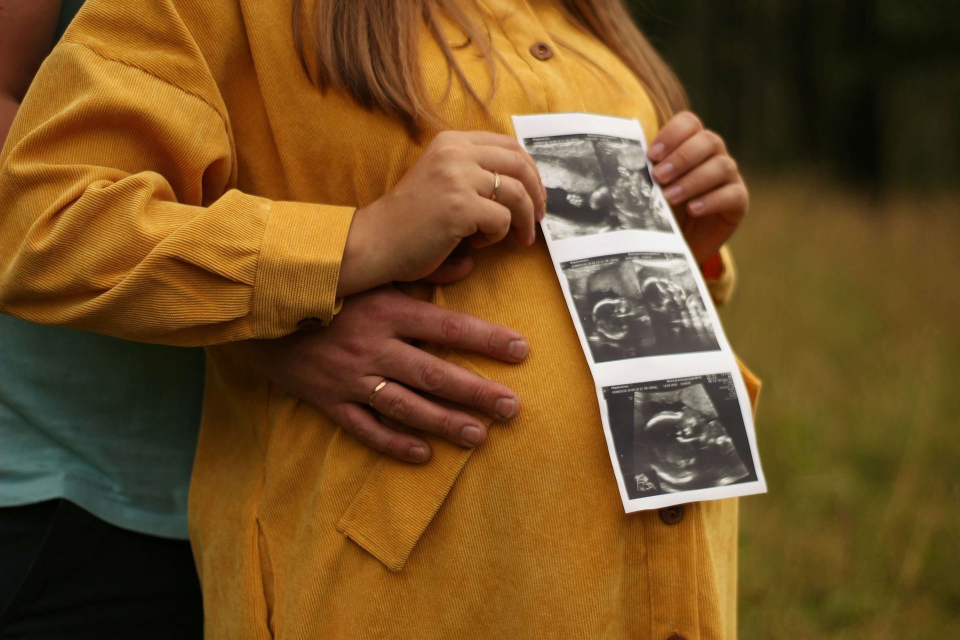 Donna incinta seduta con abito bianco, mani appoggiate sul ventre: maternit&agrave;, attesa e ricordo nel lutto perinatale